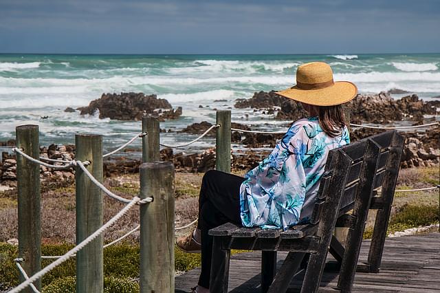 Kobieta w kapeluszu siedzi na krześle nad morzem