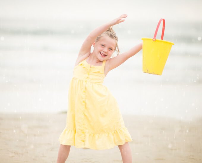 Dziewczynka w żółtej sukienkce na plaży, trzyma wiaderko